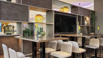 Zona de bar moderna con televisión de pantalla plana, taburetes y iluminación decorativa.