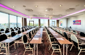Sala de conferência com mesas e cadeiras compridas, janelas amplas e vista para a cidade.