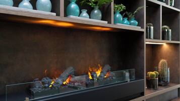 Une cheminée moderne avec une façade en verre, entourée d’étagères ornées de vases décoratifs et de plantes.