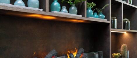 Una chimenea moderna con frente de vidrio, rodeada de estantes con jarrones decorativos y plantas.