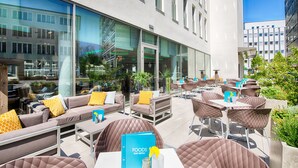 An outdoor seating area with sofas and tables, a menu board, and a view of the cityscape. - Leonardo Hotel Munich City South (Munich)