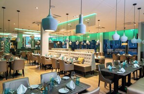 Ein modernes Restaurant-Interieur mit mehreren Essbereichen, darunter eine zentrale Lounge mit einer Sitzecke und einer Bar.