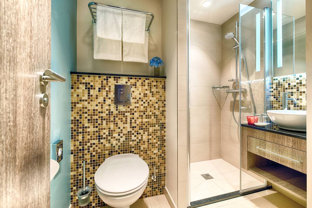 Un baño con pared de mosaicos, un inodoro, una ducha con puerta de vidrio y un lavamanos con espejo.