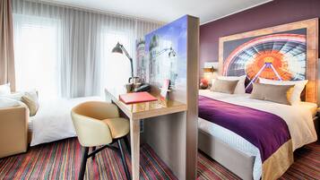 Habitación de hotel con cama, escritorio y silla, ventana con cortinas y un cuadro grande en la pared.