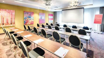 A conference room with long tables, chairs, a projector screen, and a 'Warm Welcome' sign.