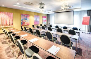 Une salle de conférence équipée de longues tables, de chaises, d’un écran de projection et d’une pancarte indiquant « Bienvenue ».