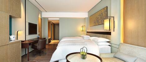 A hotel room with a bed, a desk, a chair, a sofa, and a small table with a vase.