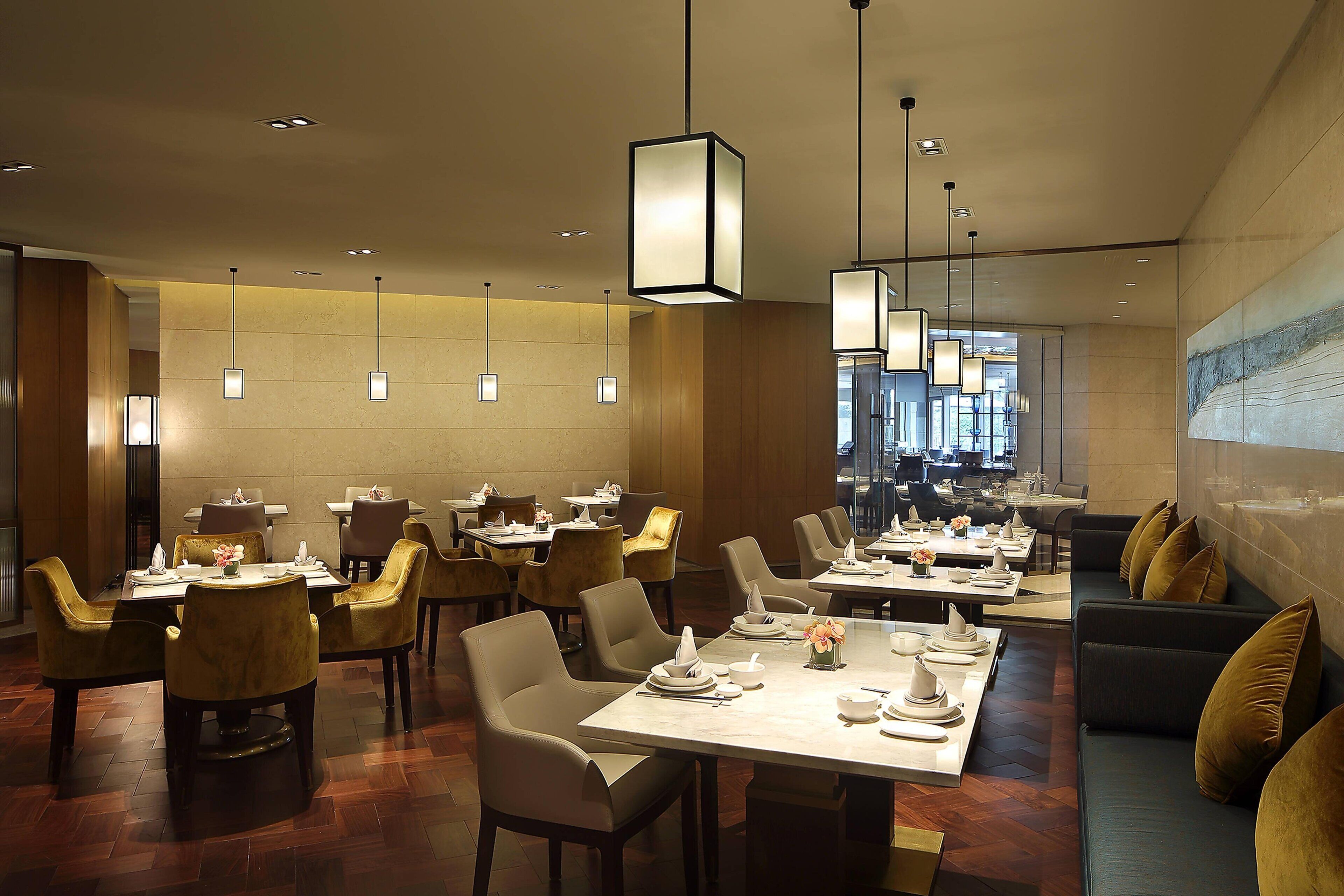 A modern dining area with multiple tables and chairs, recessed lighting, and a large window providing natural light.