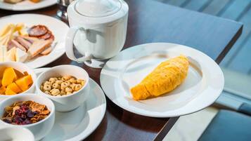 A breakfast setting with a teapot, plates of food, and bowls of cereal and fruit.