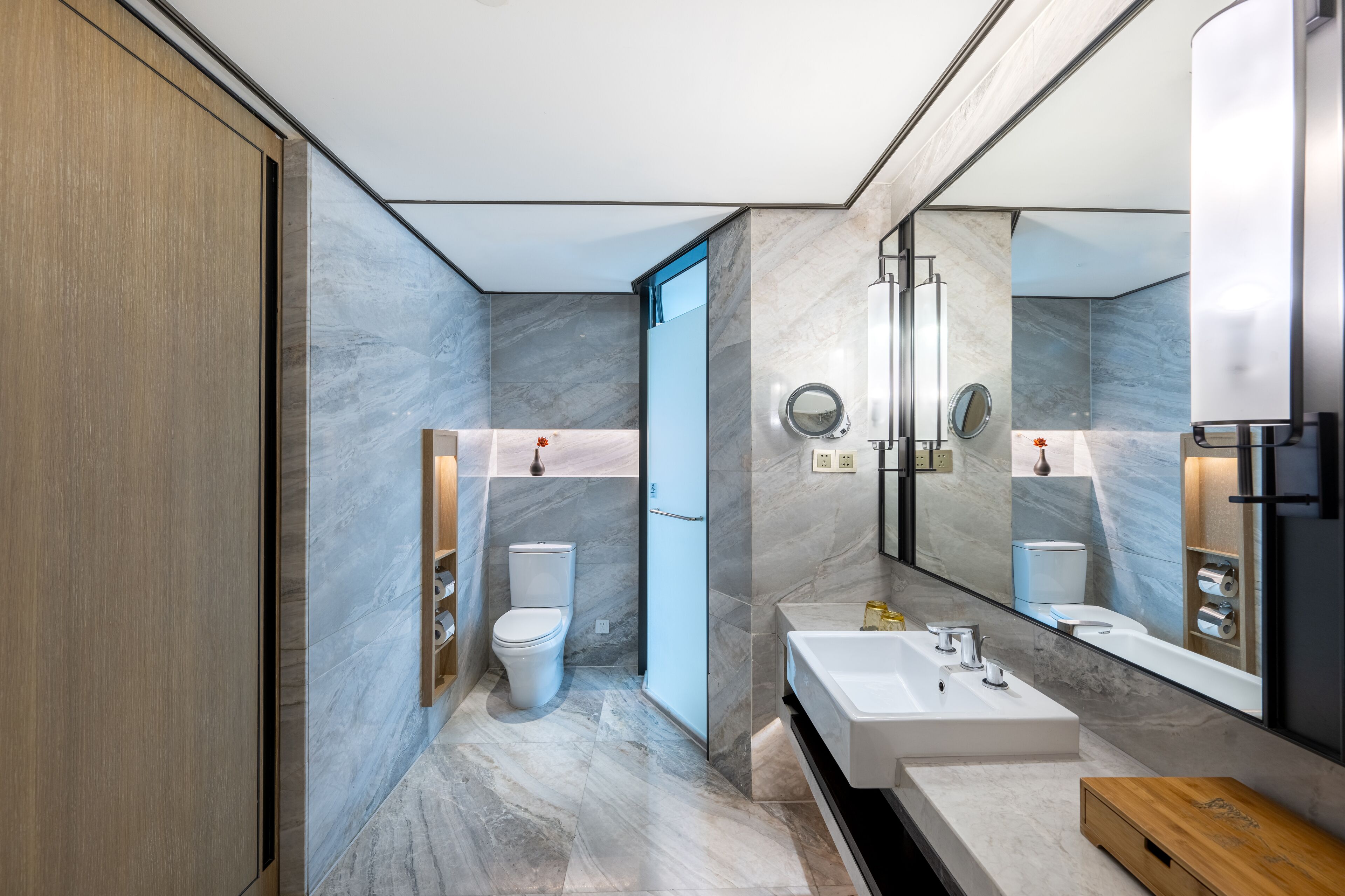 A modern bathroom with a large mirror, a bathtub, and a toilet.