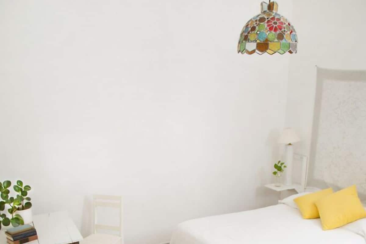 Una habitación con dos camas, un escritorio, una silla, una lámpara colgante y una pequeña mesa con una planta.