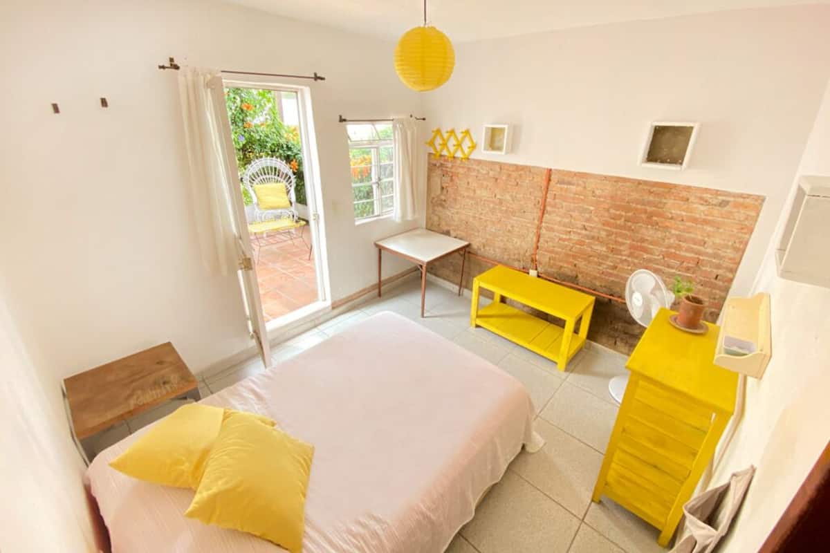 Un dormitorio con una cama, una mesita, una silla y un ventilador.