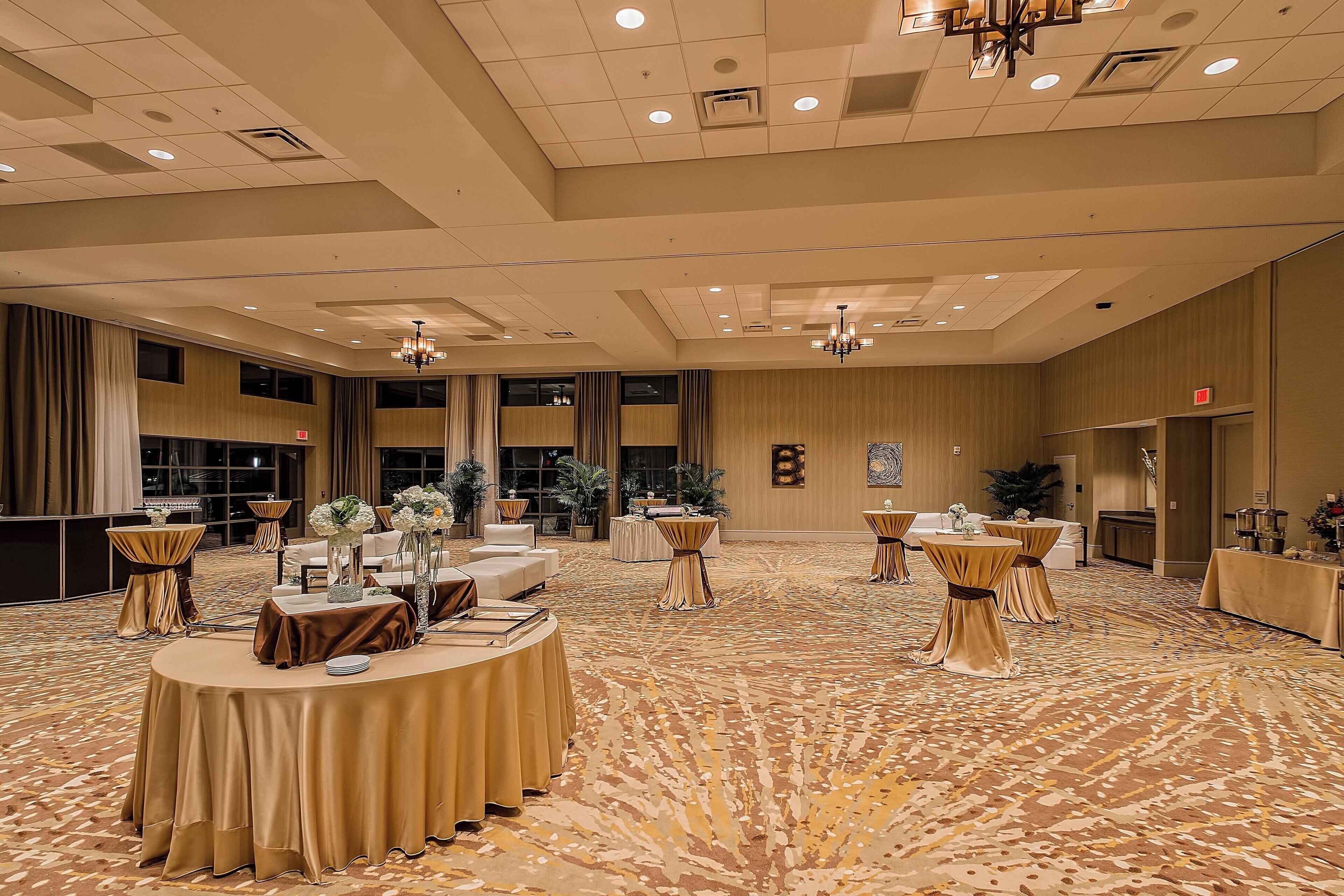 A spacious banquet hall with round tables, chandeliers, and a patterned carpet.