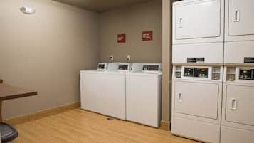 Een wasserette met gestapelde wasmachines en drogers, een afvalbak en een brandmelder aan de muur.