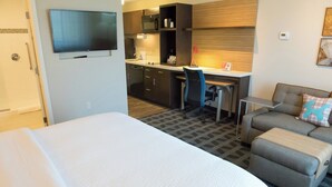 Une chambre d’hôtel avec un grand lit, un bureau avec une chaise, une kitchenette et un canapé.