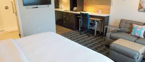 A hotel room with a large bed, a desk with a chair, a kitchenette, and a sofa.