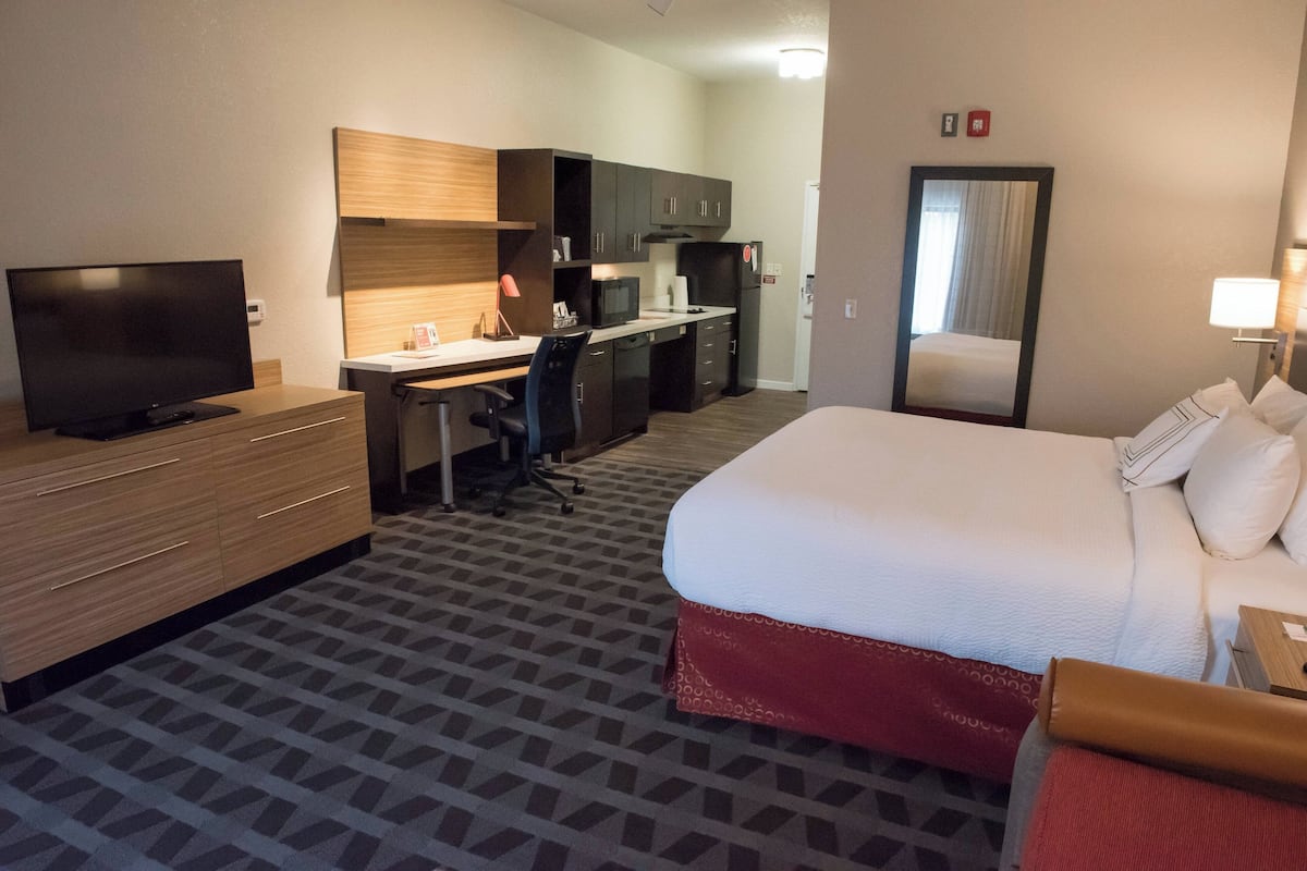 Ett hotellrum med en säng, ett skrivbord med en stol, en tv, en mikrovågsugn och ett litet kök.