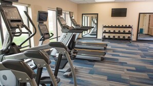 Une salle de sport équipée de tapis de course, de vélos elliptiques et d’une série de haltères.