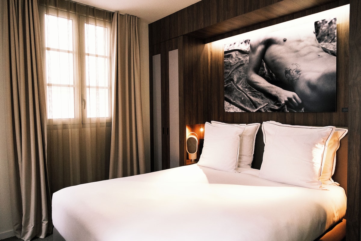 A hotel room with a large bed, beige curtains, a wall-mounted mirror, and a framed picture on the wall.