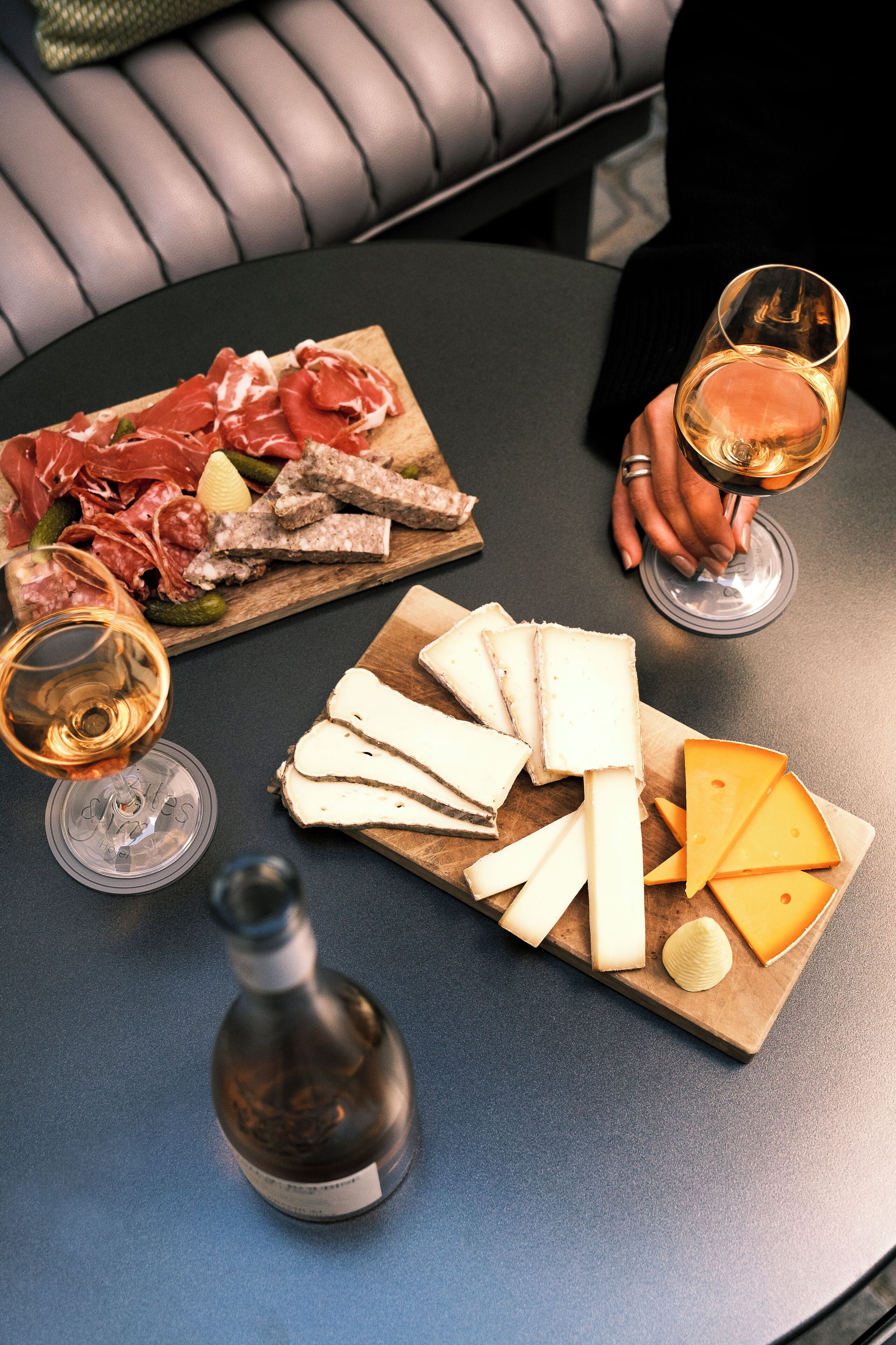 Una mesa con varios quesos, embutidos y una botella de vino, evocando una degustación de quesos o una comida informal.