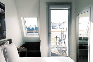 A hotel room with a bed, a small table with a book, a chair, a window with a view of the city, and a balcony with chairs and a table. - Hotel Jules & Jim (Paris)