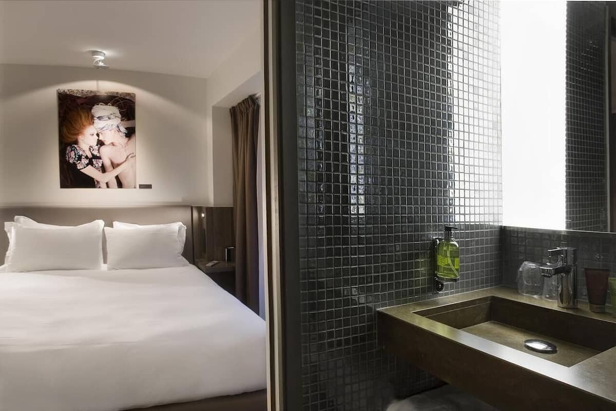 A hotel room with a large bed, a wall-mounted artwork, and a bathroom with a tiled backsplash and a sink.