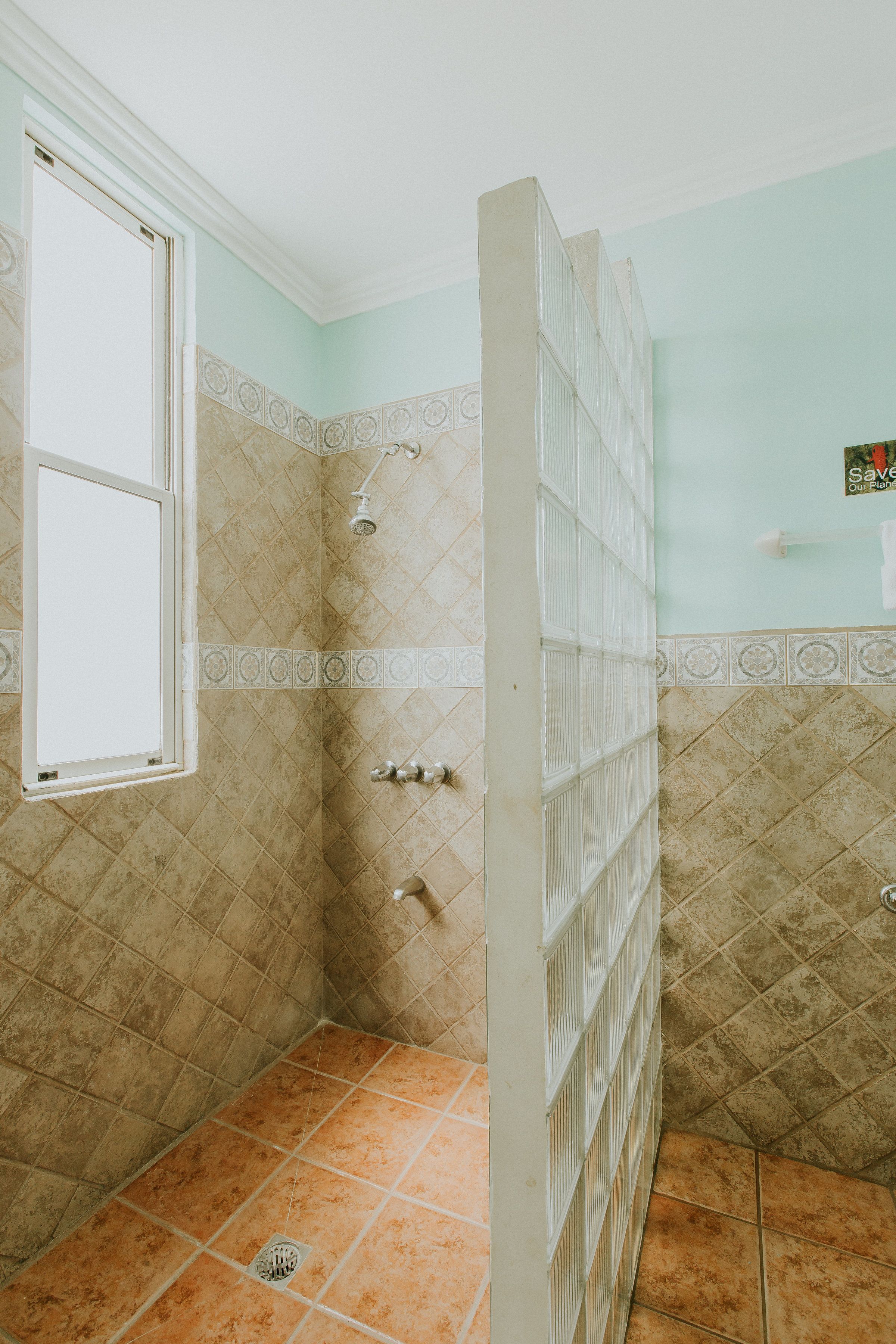 A bathroom with a shower, a window, and a tiled floor.