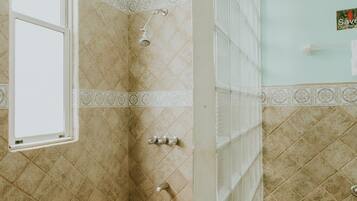 Un baño con ducha, ventana y piso de baldosas.