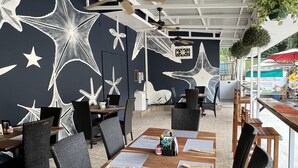 An outdoor restaurant with tables and chairs, ceiling fans, and a mural with star designs. - Hotel La Posada and Jungle (Quepos)