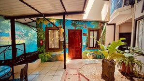 A covered patio with a tiled floor, a wooden door, and a mural of a tropical scene. - Hotel La Posada and Jungle (Quepos)