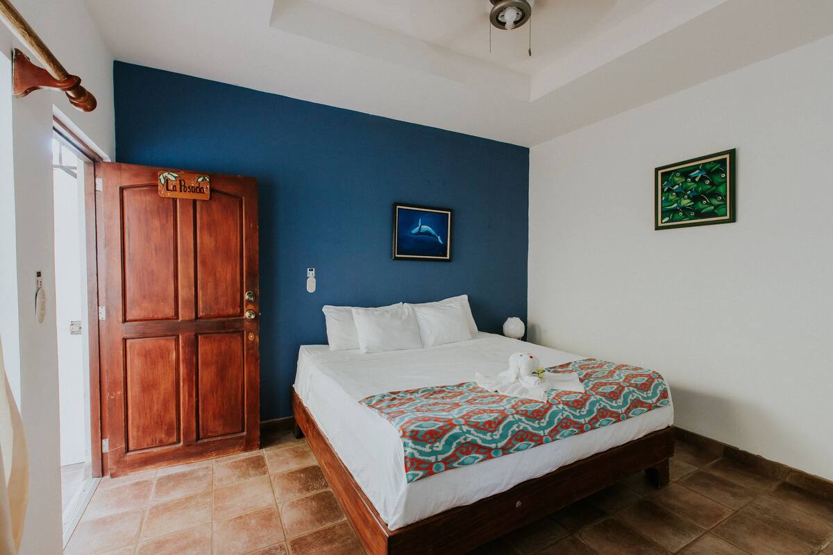 A bedroom with a wooden door, a bed with white bedding, a blue wall, and a framed picture of a dolphin.