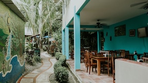 A restaurant with outdoor seating, a tiled floor, and a mural on the wall. - Hotel La Posada and Jungle (Quepos)