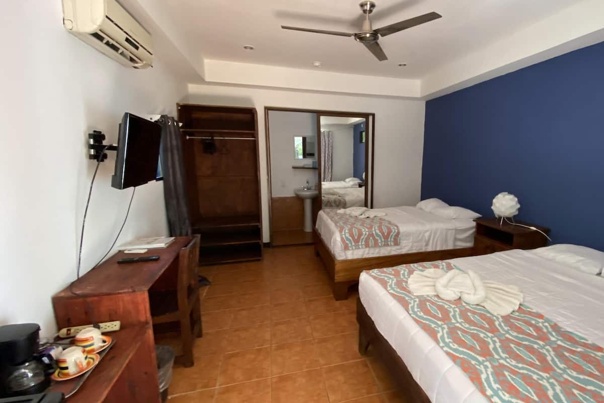 A hotel room with two beds, a desk with a chair, a television, and a ceiling fan.