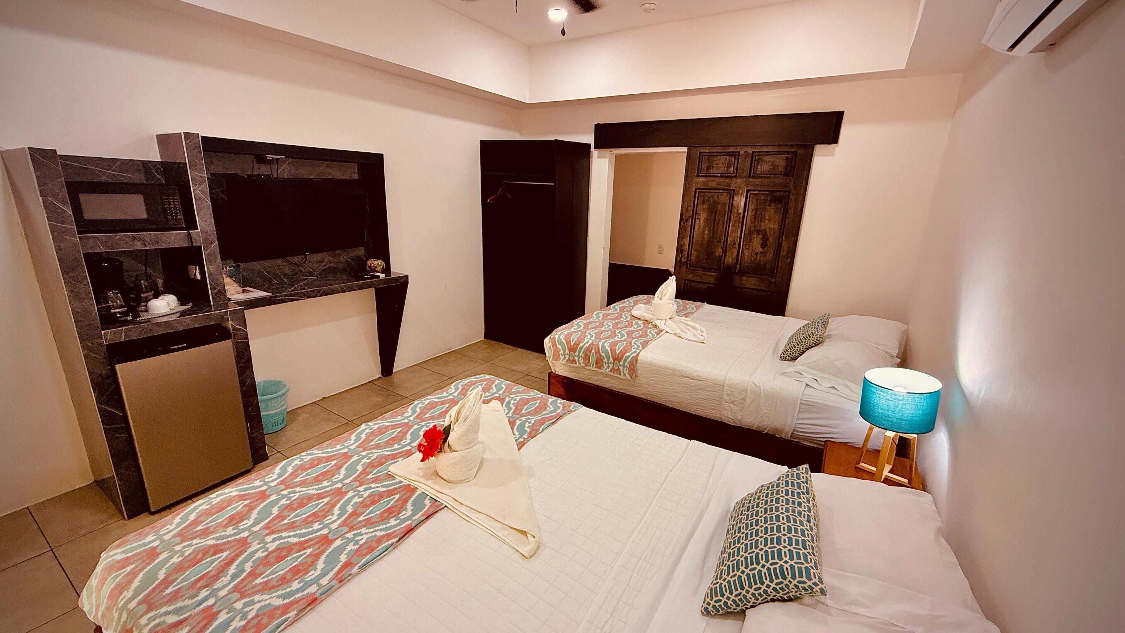 Quarto de hotel com duas camas, uma secretária pequena com espelho, guarda-roupa e banheiro.
