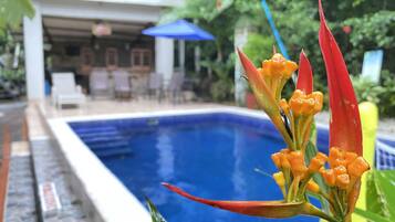 A swimming pool with a clear blue water surface, surrounded by a poolside area with lounge chairs and a covered seating area.