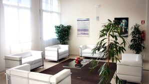 Una sala de estar moderna y bien iluminada, con muebles blancos, una mesa de centro de vidrio y ventanas amplias.