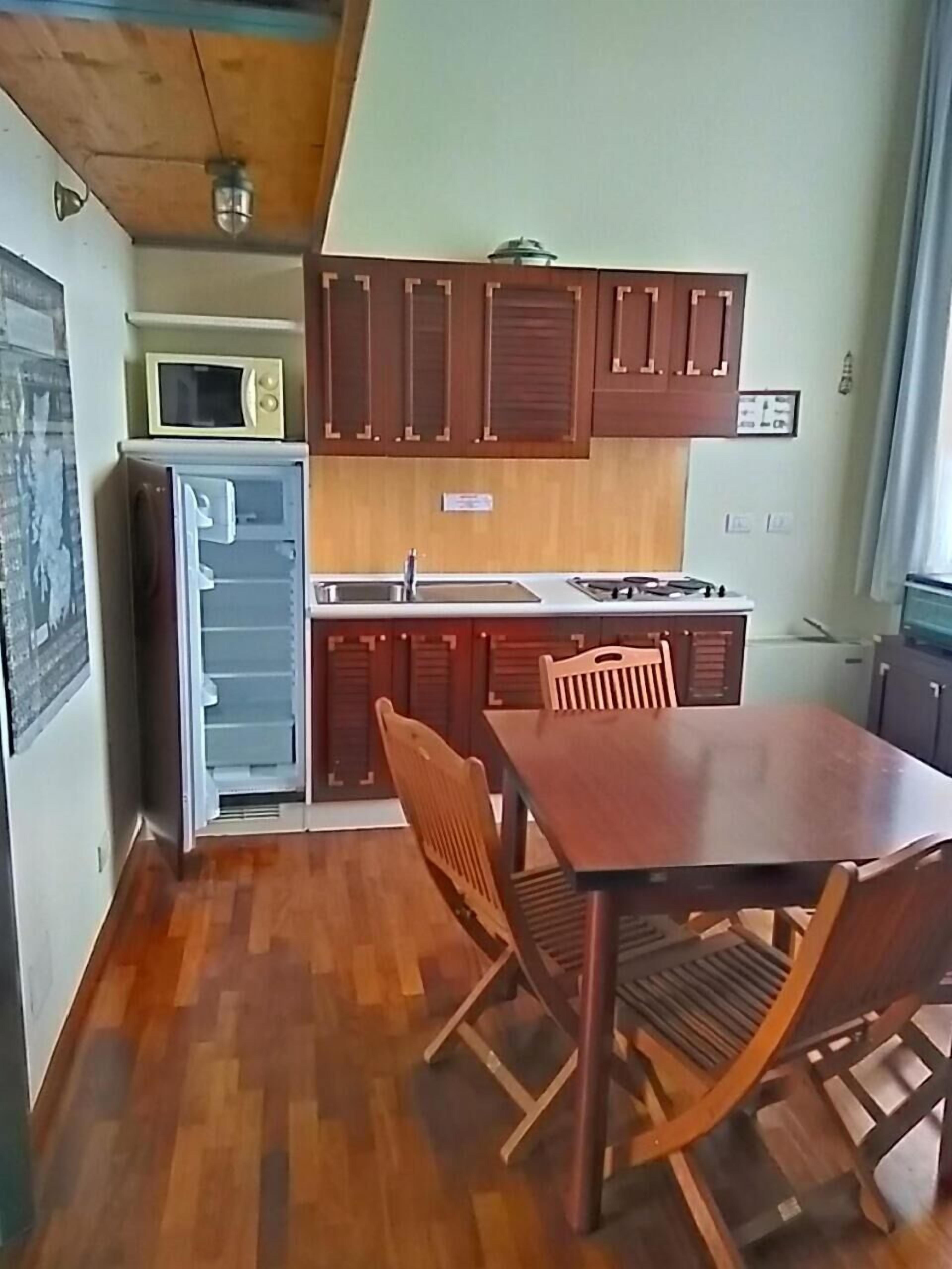 A compact kitchen with wooden cabinets, a microwave, a refrigerator, and a dining table with chairs.