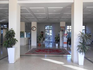 Een ruime lobby met een groot rood tapijt, potplanten en een klok aan de muur.