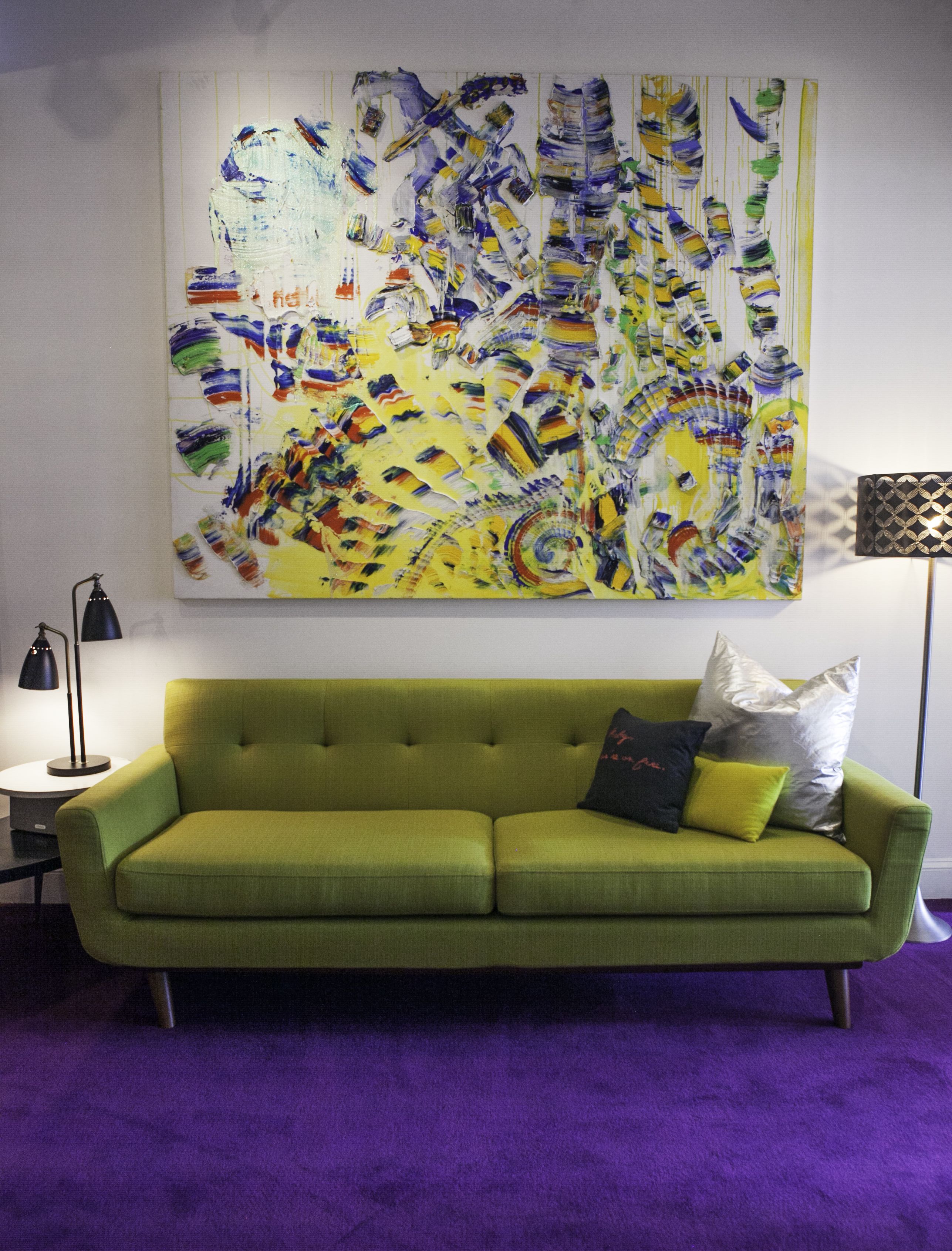 A green sofa with a cushion, a lamp, and a large abstract painting on the wall.