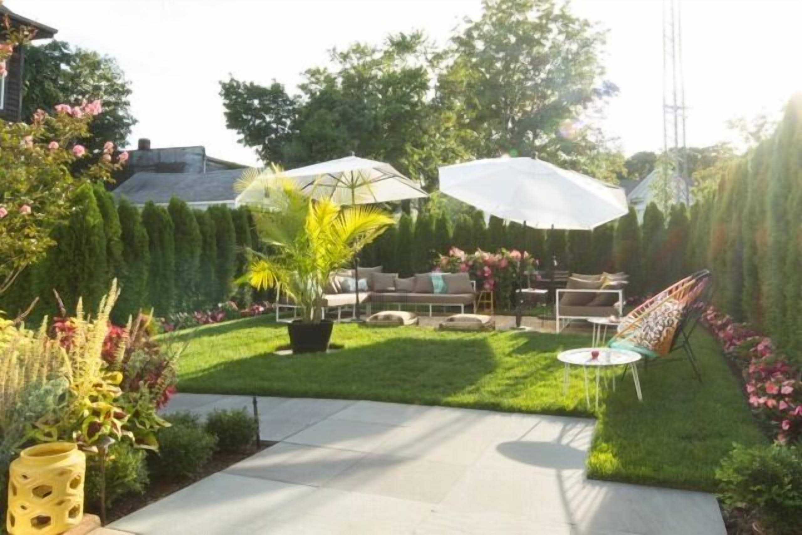 A backyard with a lawn, patio furniture, and potted plants.