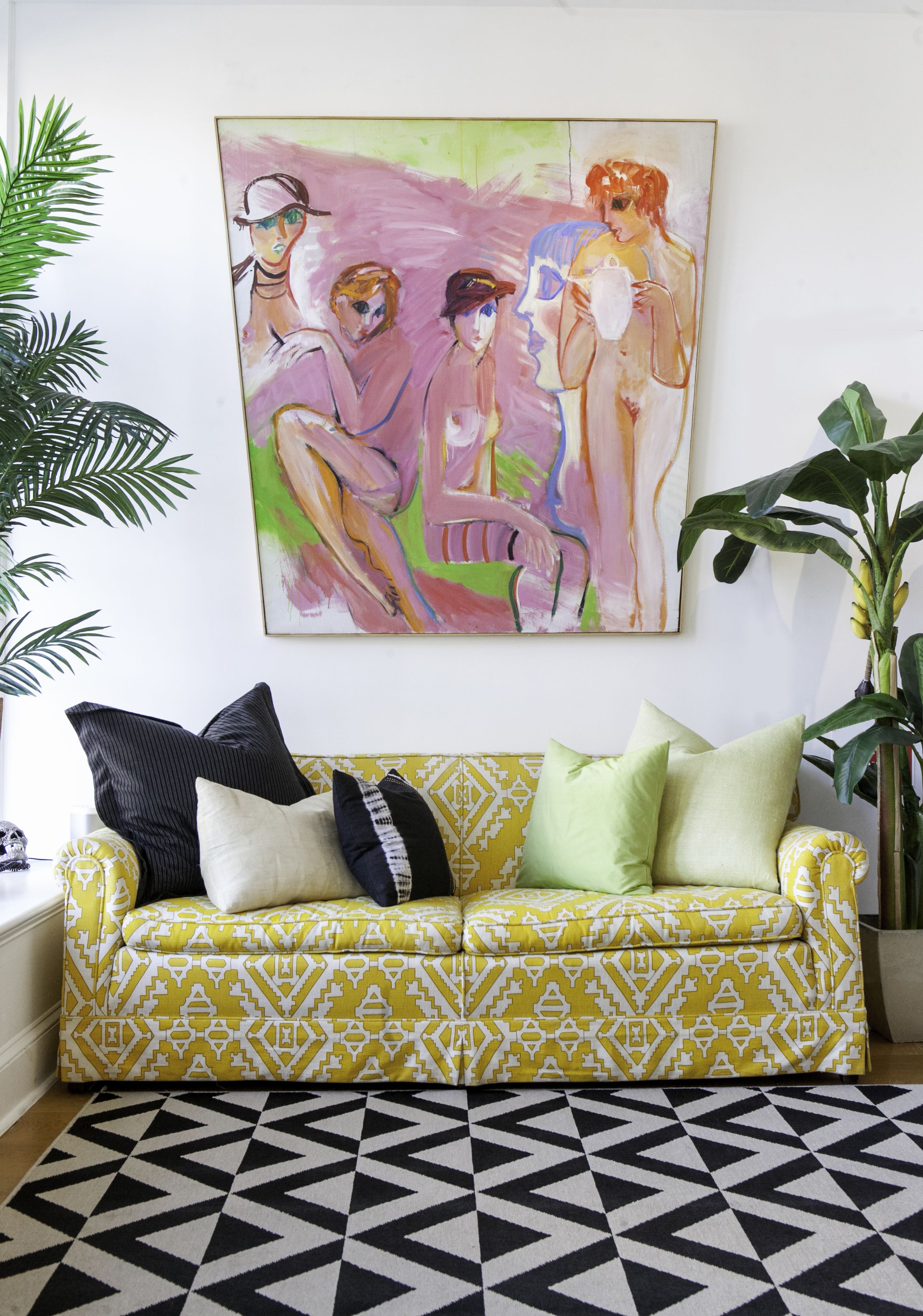 Ein gelbes, gemustertes Sofa mit schwarzen und weißen Kissen, ein geometrischer Teppich und ein großes abstraktes Gemälde an der Wand.