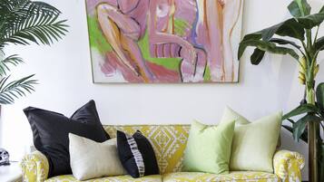Un divano giallo con motivo decorativo, cuscini bianchi e neri, un tappeto a motivi geometrici e un grande quadro astratto appeso al muro.