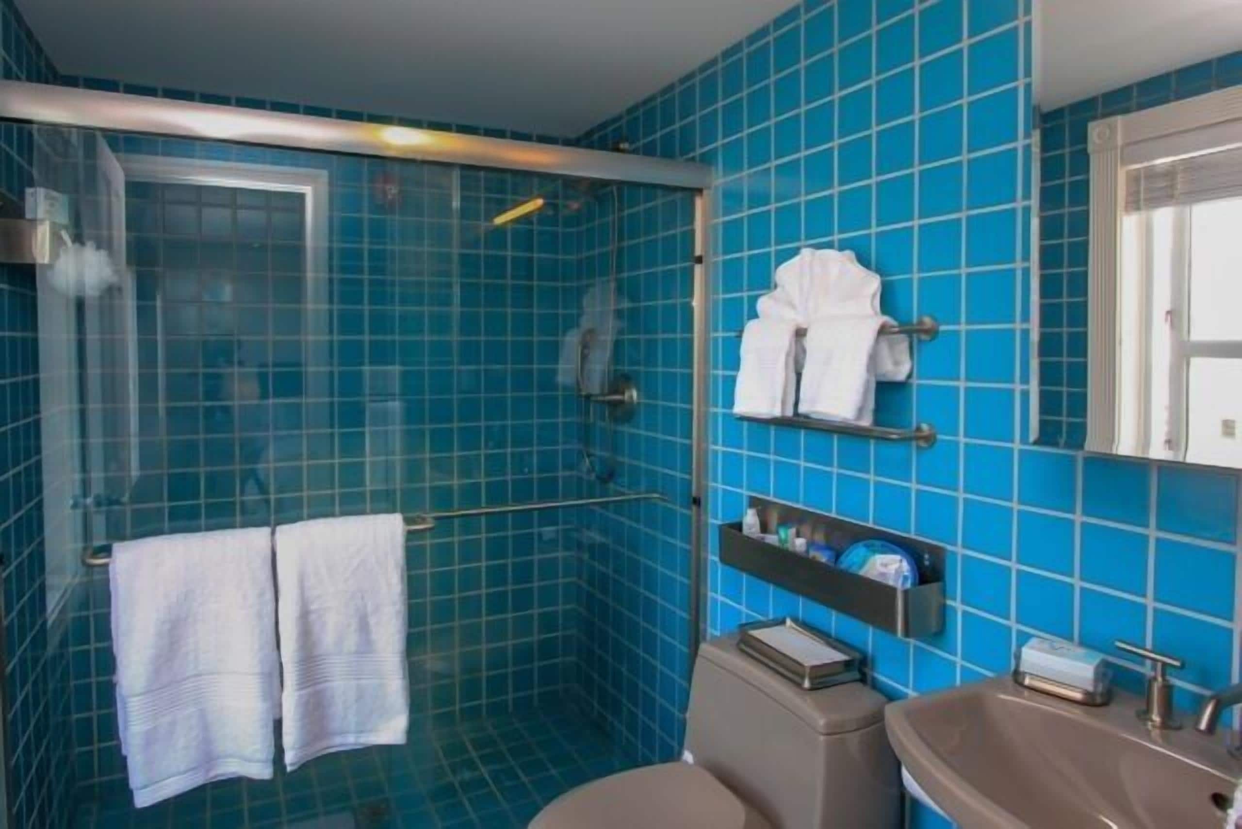 Une salle de bain avec des carreaux bleus, une douche en verre, des toilettes, un lavabo et un porte-serviettes avec des serviettes.