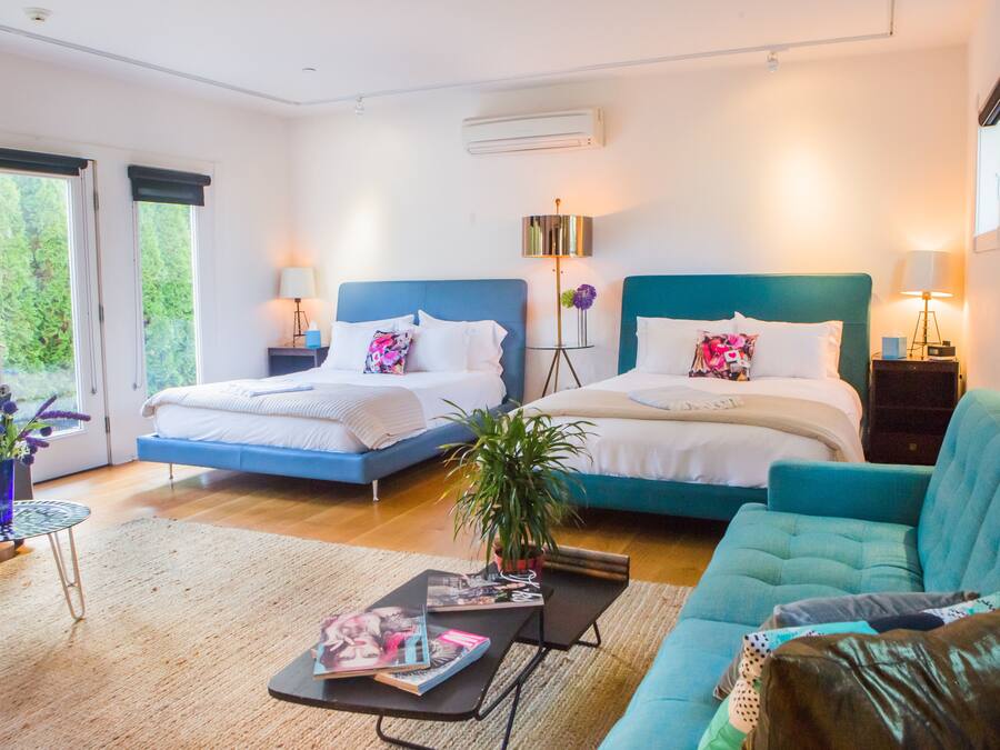A modern bedroom with two beds, a sofa, a coffee table, and a potted plant.