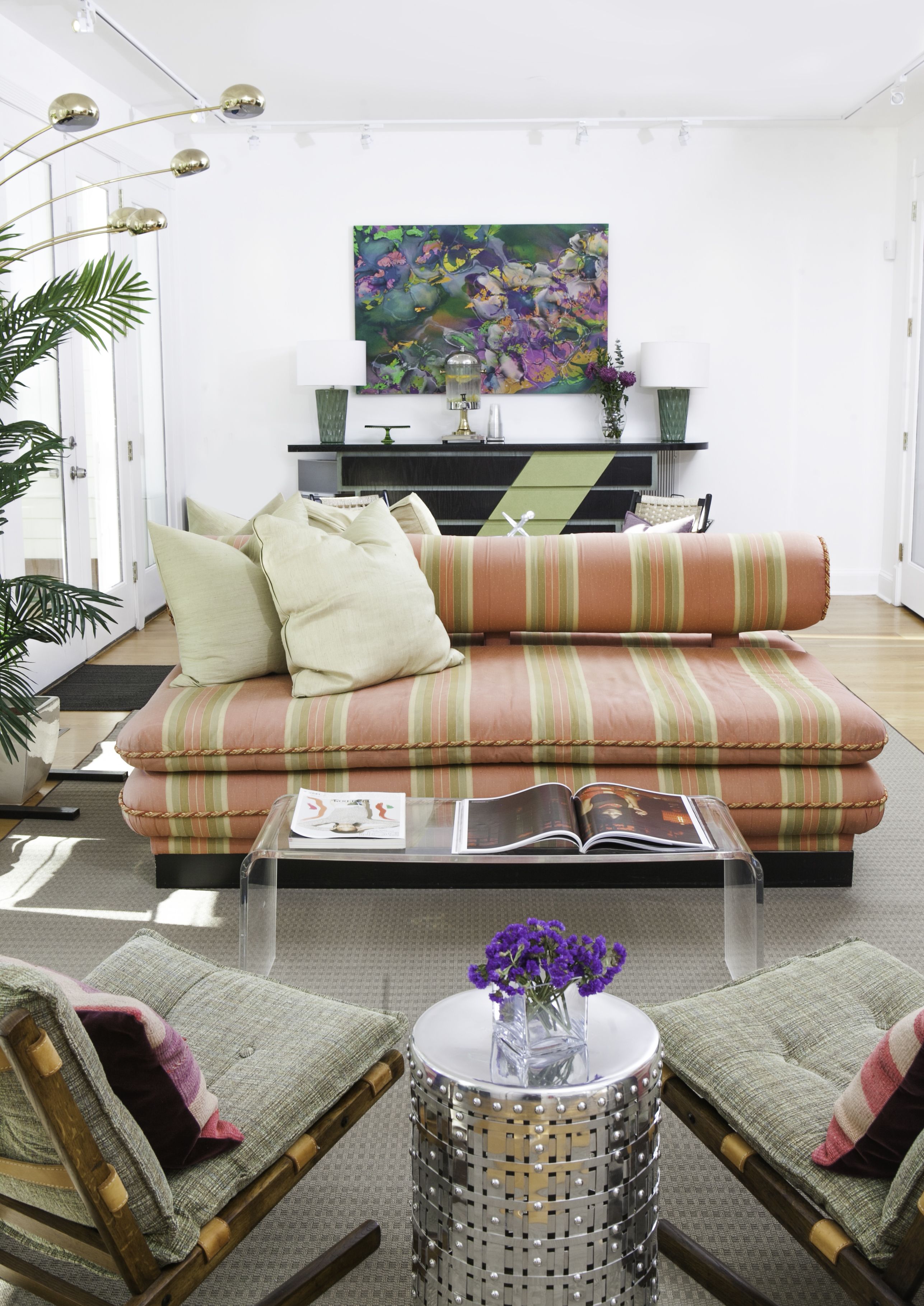 A modern living room with a striped sofa, two armchairs, a coffee table, and a painting on the wall.