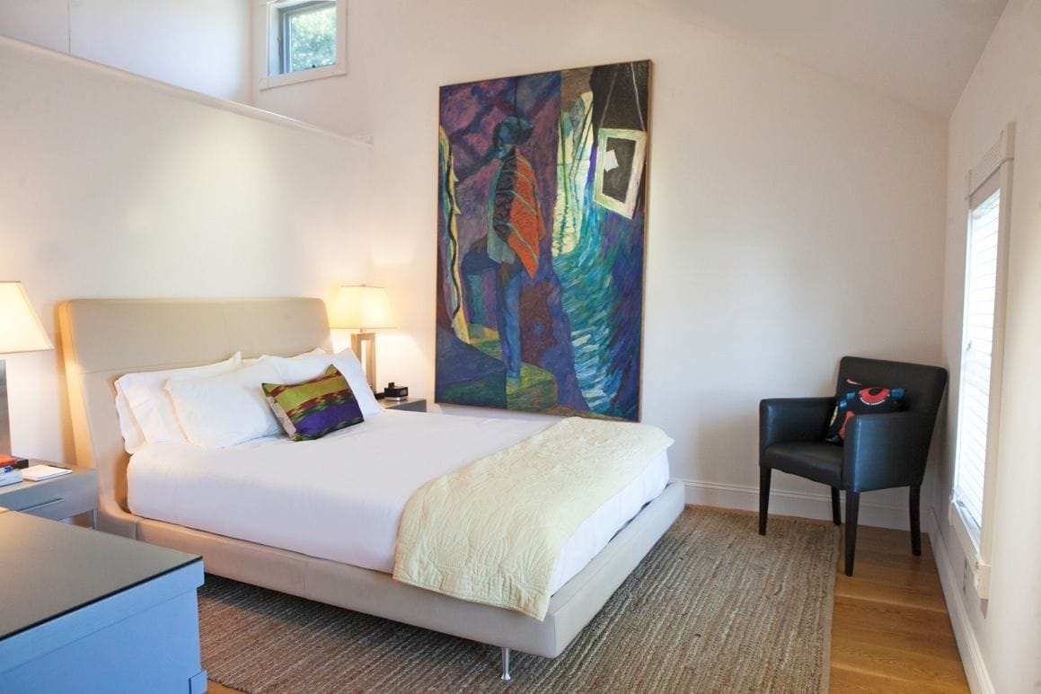 A modern hotel room with a large bed, a chair, and a colorful abstract painting on the wall.