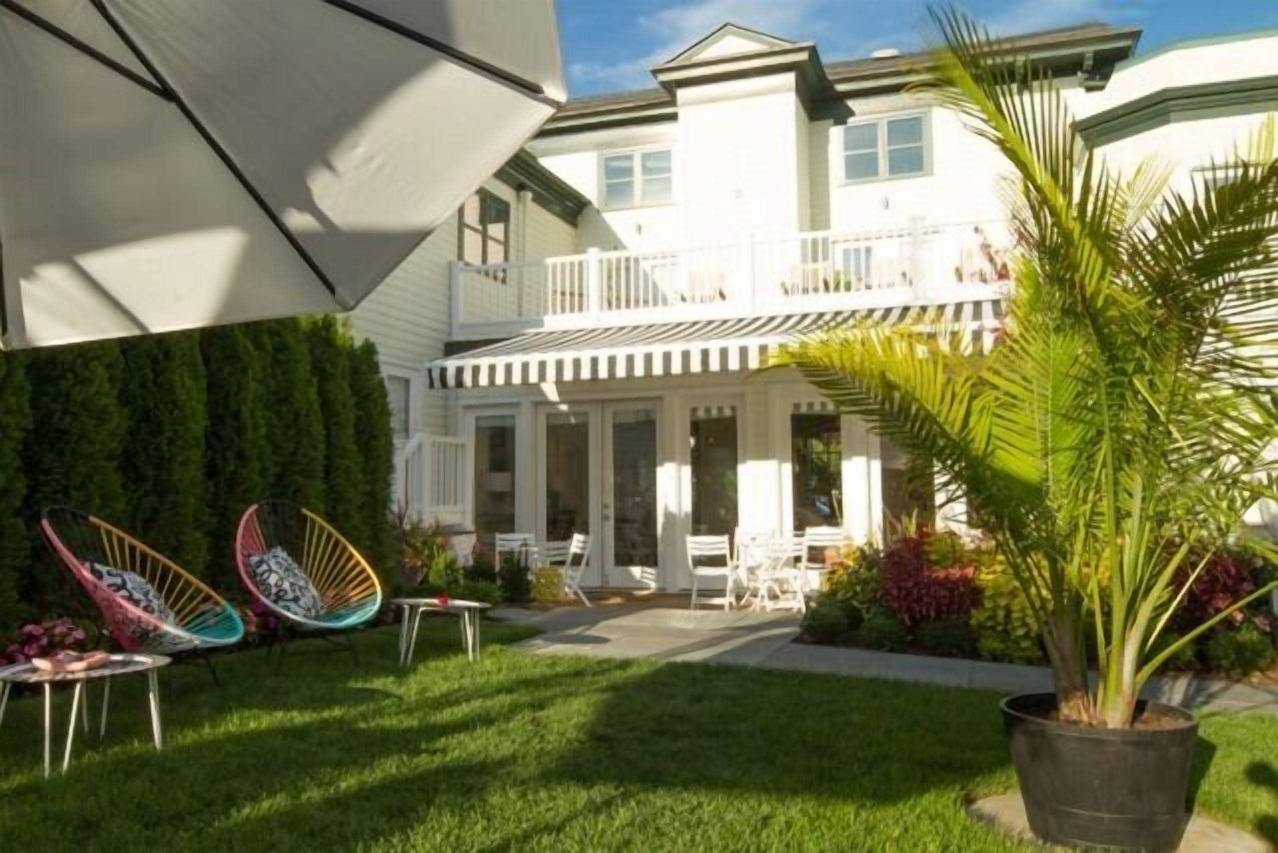A two-story house with a balcony, a lawn, and outdoor furniture.