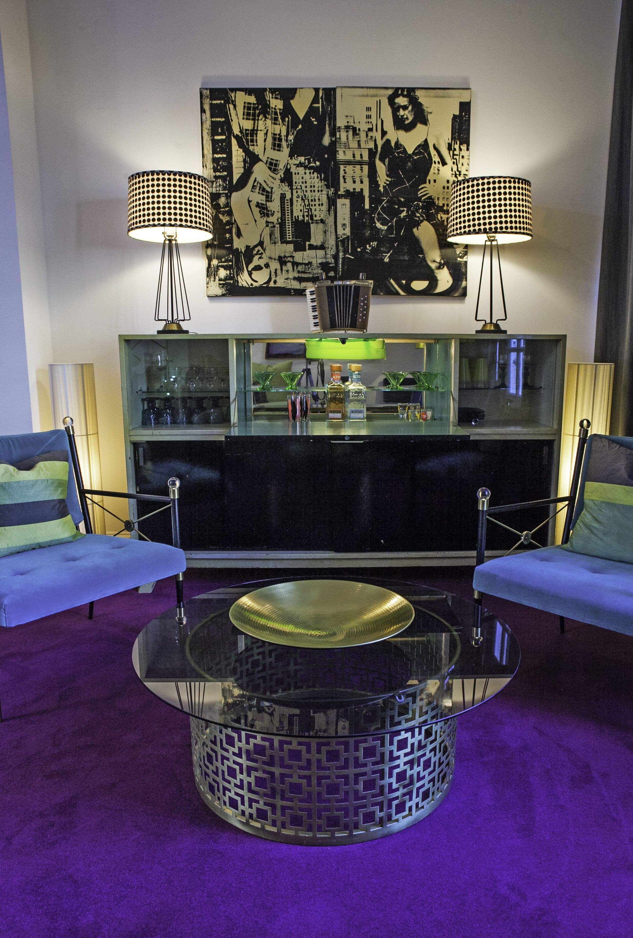 A modern living room with two sofas, a glass coffee table, and a bar area with a cityscape painting above.