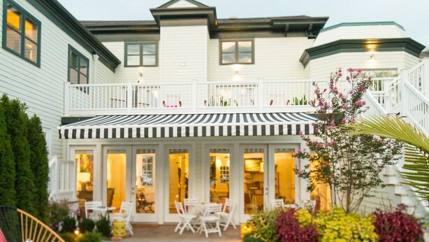 A two-story house with a balcony, outdoor seating area, and a variety of plants. - Zey Hotel (Greenport)