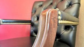 Primer plano del reposabrazos de madera de una silla, con un respaldo de cuero y remaches metálicos.